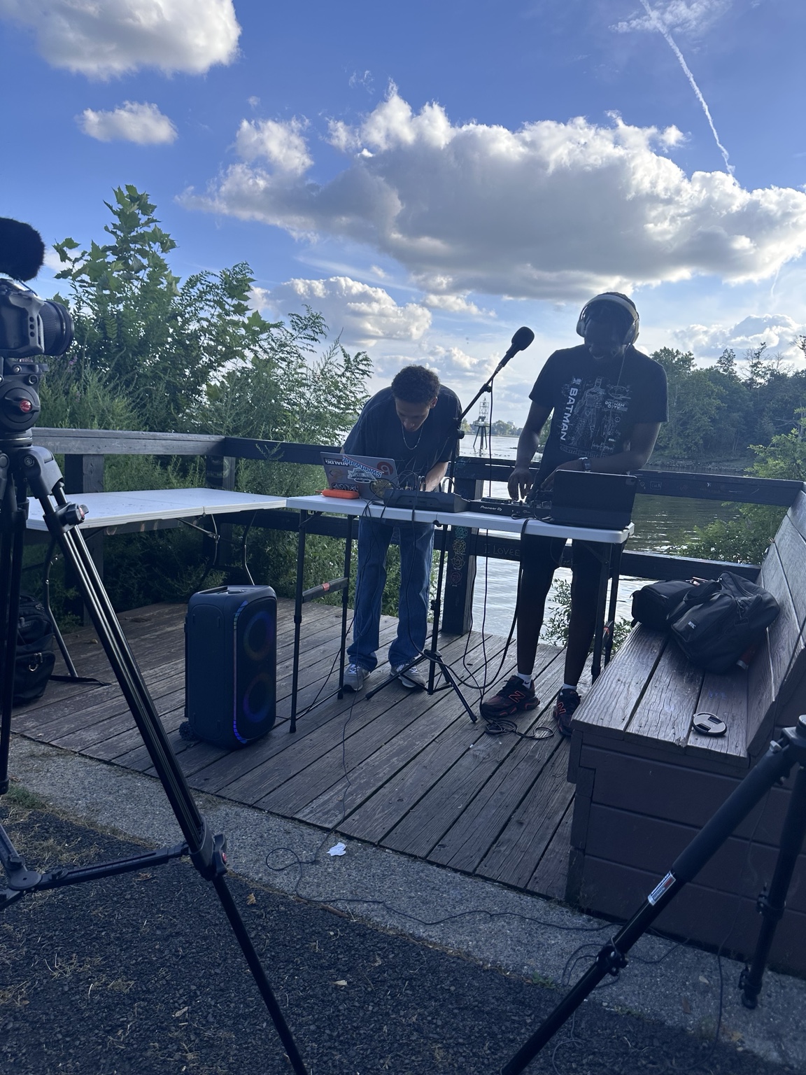 DJ JT mixing on an outdoor wooden deck beside the water